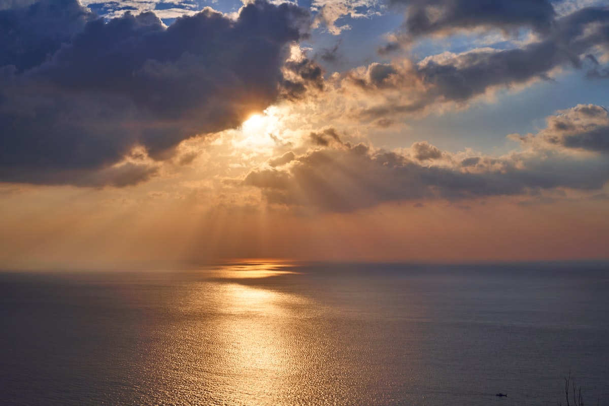 Sunlight breaking through dramatic clouds over a calm sea, symbolising hope and the coming of the Holy Spirit